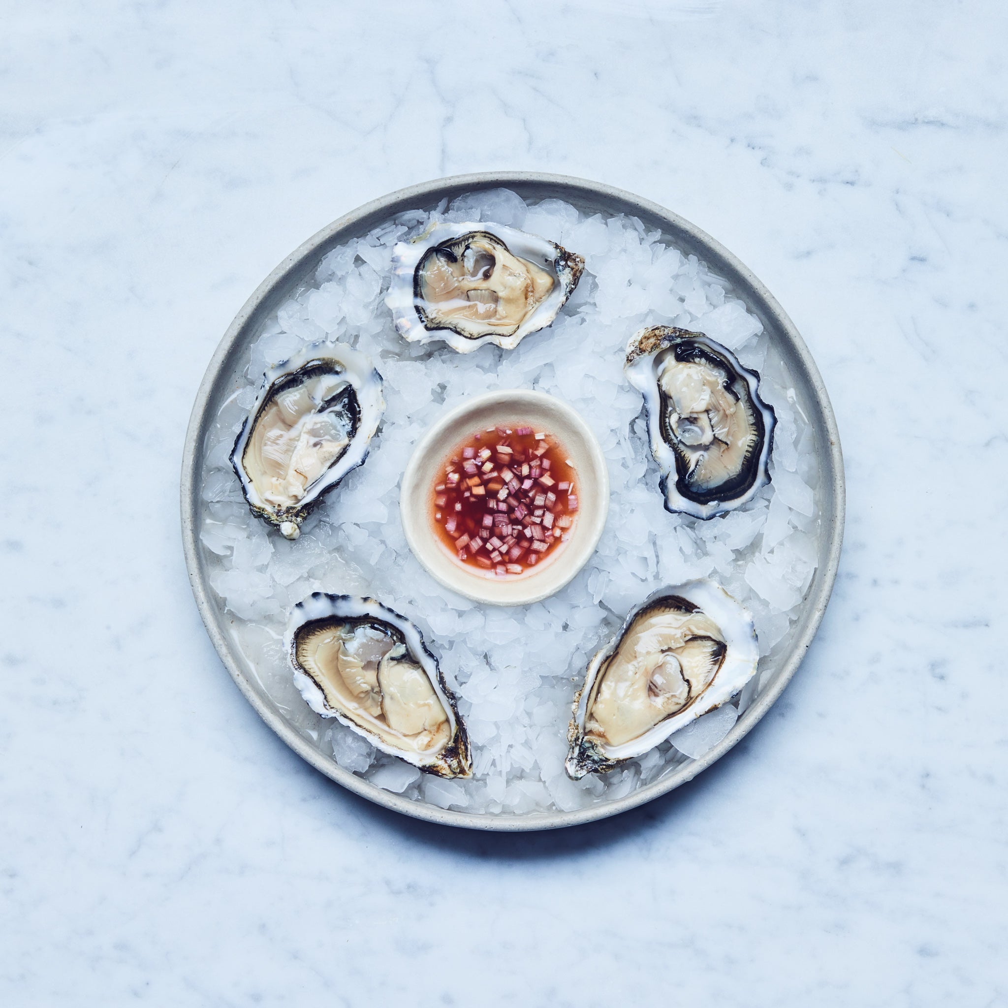 Fünf frisch geöffnete Gilleardeu Austern auf Eis mit Soße auf einem Teller, von Frisch Gefischt. Gillardeau austern kaufen.