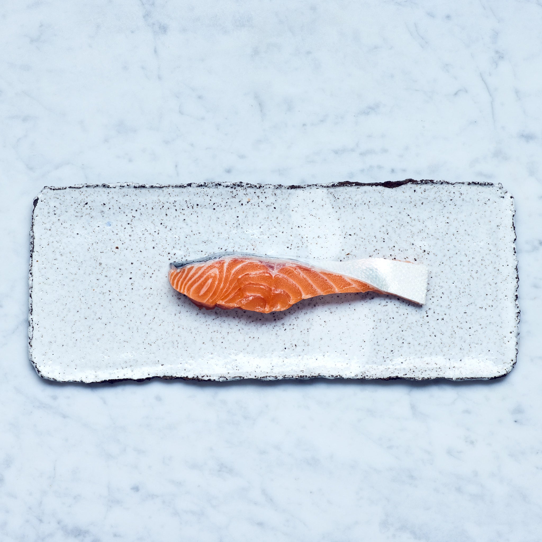 Lachsfilet kaufen. Ein Stück frischer Lachs in Fischform auf einem weißen Teller.