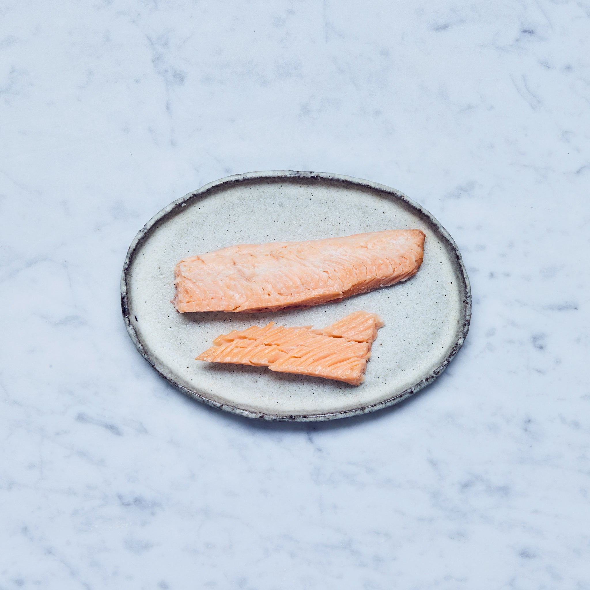 Zwei Stücke geräuchertes Lachsforellenfilet von Frisch Gefischt auf einem Teller auf einer Marmoroberfläche.