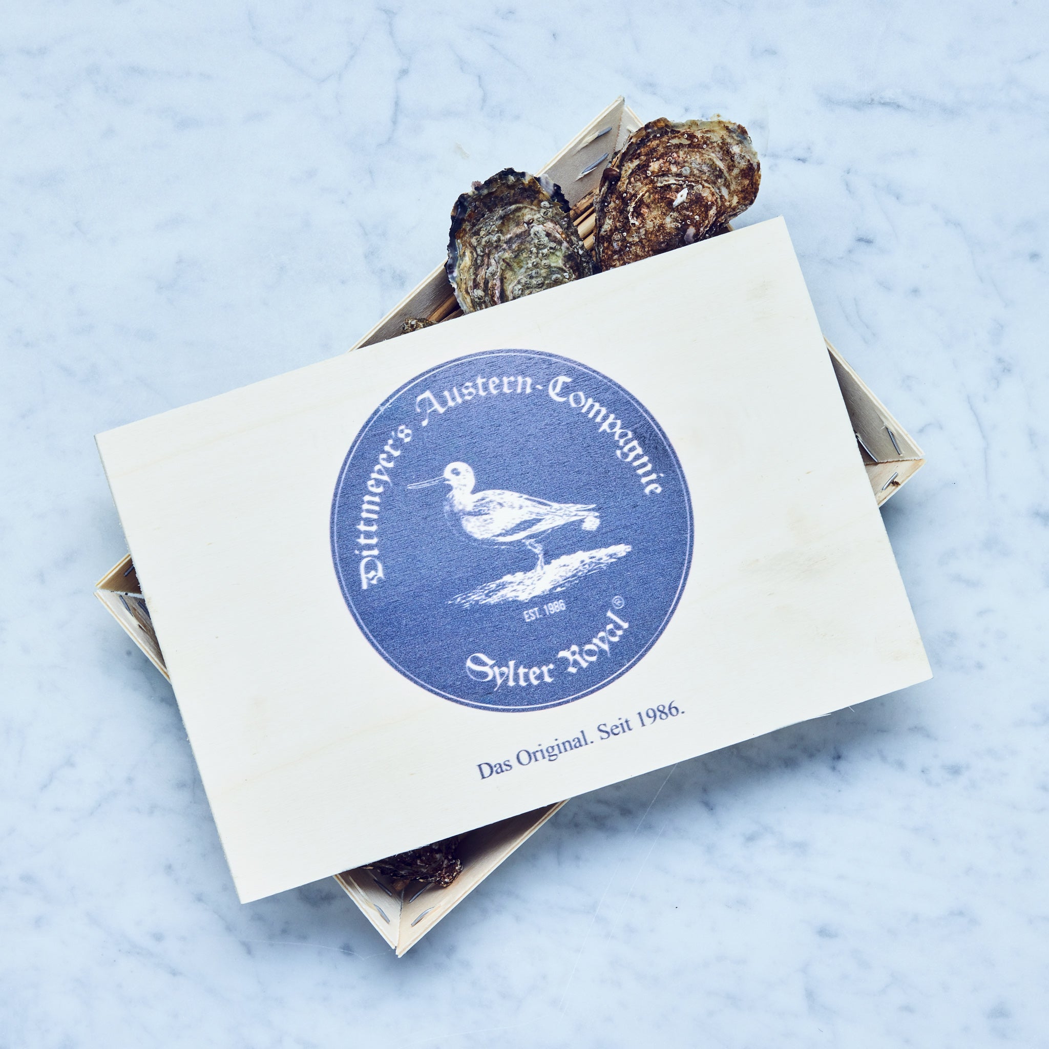 Frische Sylter Royal Austern in einer hölzernen Box mit einem blauen Label.